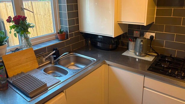 A modern kitchen with a double sink, a stove, and a window with a view of a wooden fence. - 3 Bedroom House Sleeps 5 -private Garden -parking (Leeds)