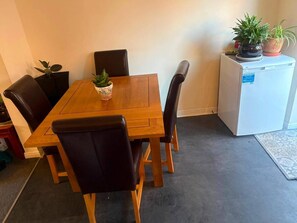 Ein Essbereich mit einem Holztisch, vier Stühlen und einem Kühlschrank, der mit Blumentöpfen dekoriert ist.