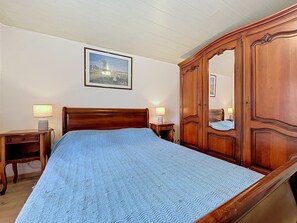 Ein Schlafzimmer mit einem hölzernen Bett, zwei Nachttischen mit Lampen, einem großen Kleiderschrank und einem gerahmten Bild an der Wand.