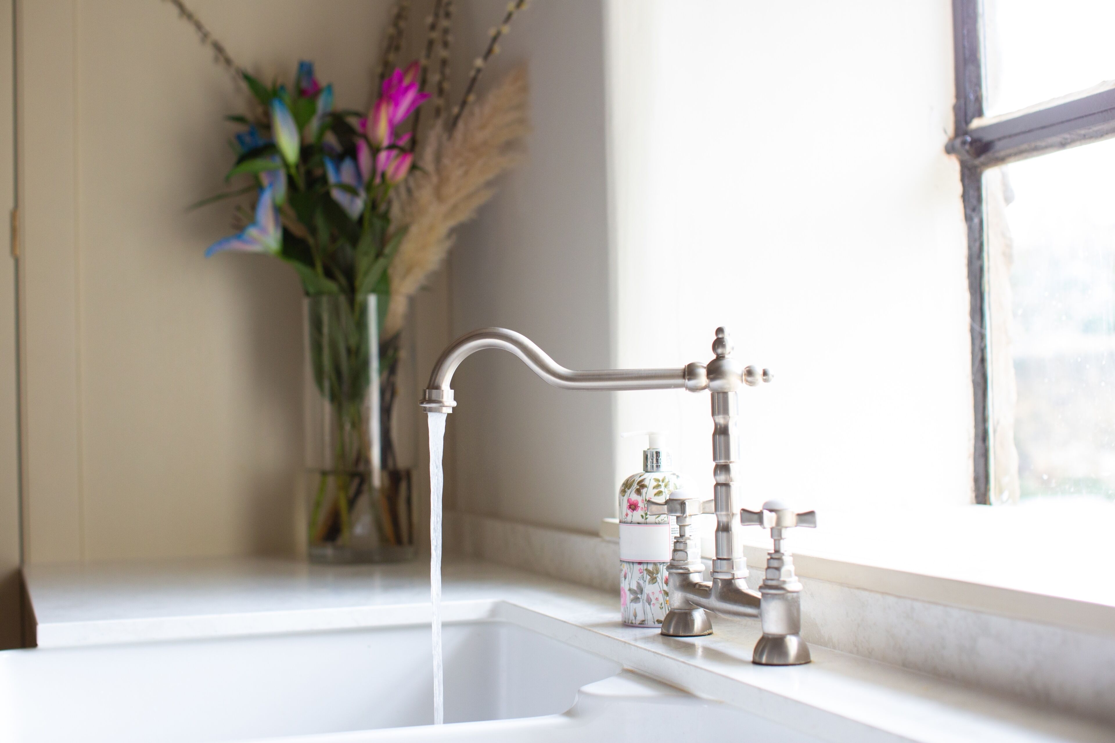 A bathroom sink with a running faucet, a soap dispenser, and a window with a view of the outdoors.