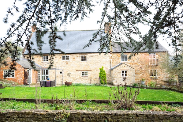 A stone house with a sloped roof, multiple windows, and a well-maintained lawn.