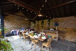 An outdoor dining area with stone walls, wooden furniture, and hanging light bulbs.