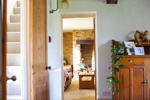A room with a wooden door, a staircase, a stone wall, a wooden cabinet with a plant, and a small table with a vase.