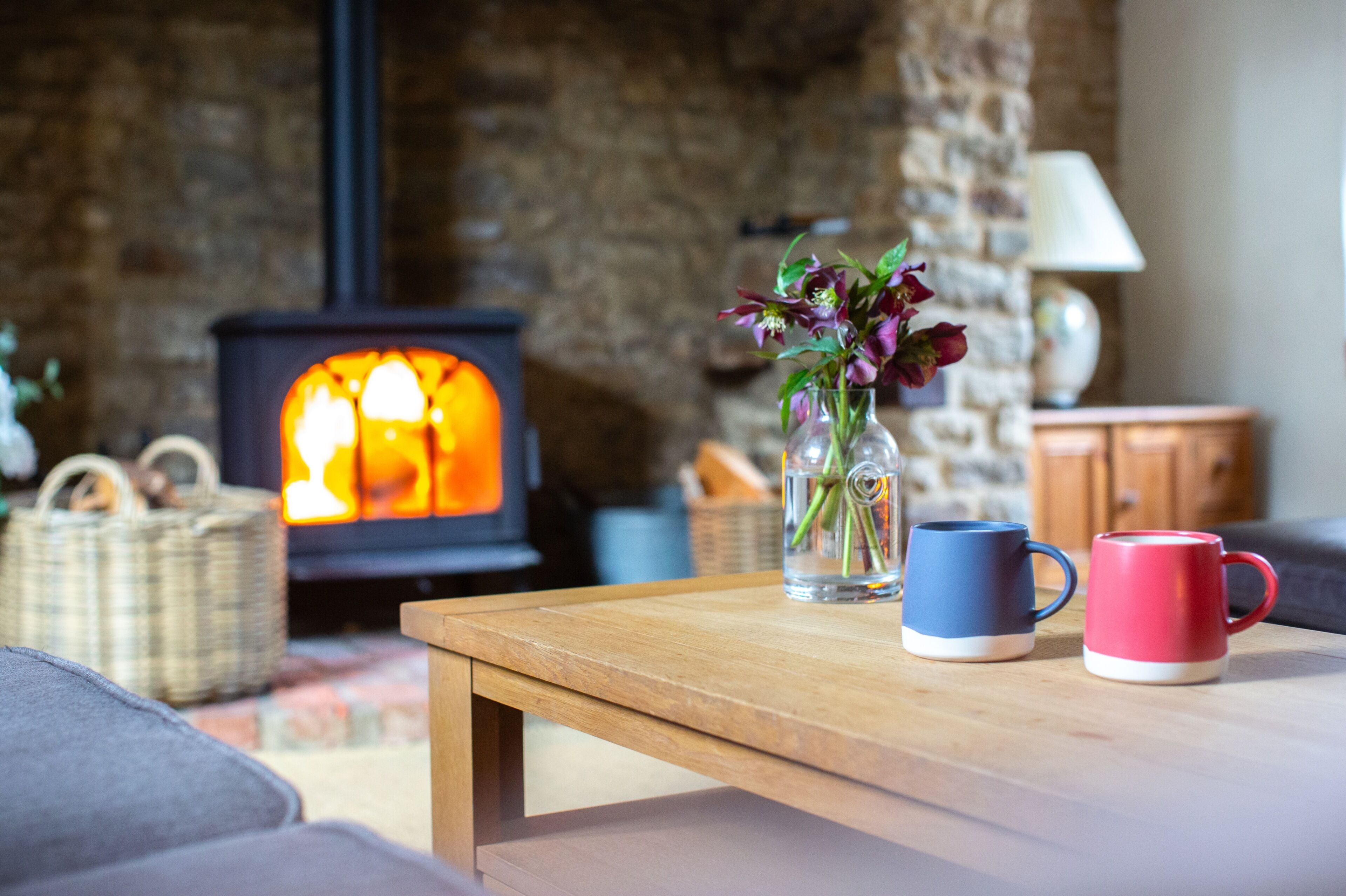 A cozy living room with a fireplace, a wooden coffee table, and a vase with flowers.