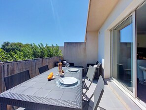 Ein Essbereich im Freien mit einem Tisch für zwei Personen, Stühlen und einer Glastür, die zu einer Küche führt.