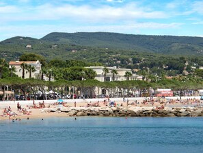 Una playa con gente tomando el sol y nadando, una costa rocosa y edificios al fondo.