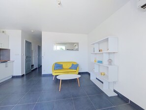Una sala de estar moderna con un sofá amarillo, una mesa de centro redonda y una consola blanca con estantes.