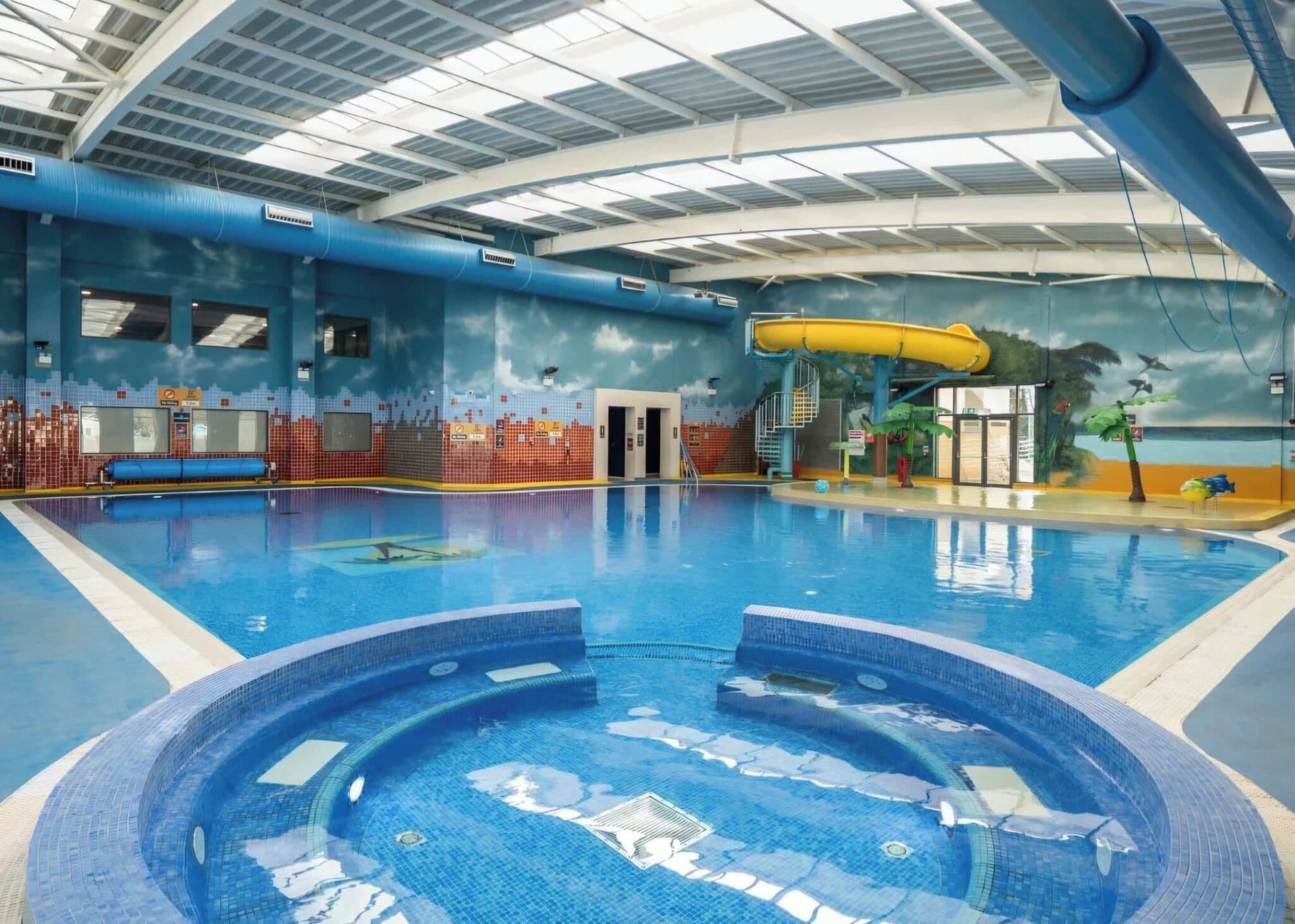 Una piscina interior con jacuzzi, toboganes y un mural con motivos tropicales.