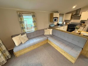 A compact living space with a sofa, a kitchenette, and a window with curtains. - Billing Aquadrome Holiday Park - 2 Bedroom, Silver (Northampton)