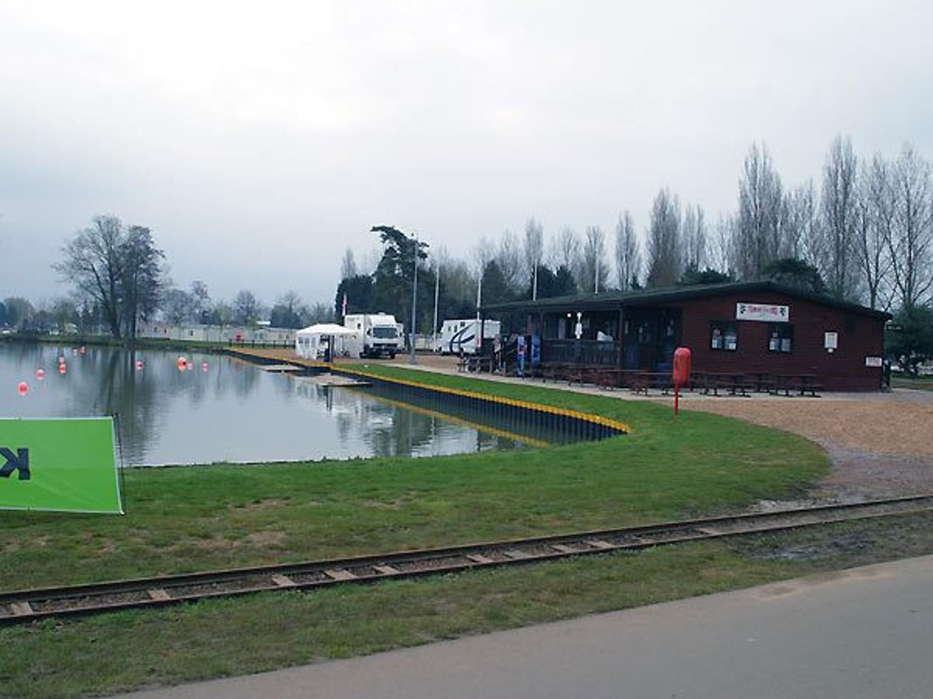 Ein Bahnhof am Seeufer, mit einer grünen Schilder und einem roten Gebäude, sowie einer grünen Wiese.