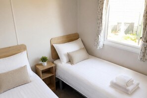 Ein Einzelbett mit Holz Kopfteil, ein Nachttisch mit Pflanze und ein Fenster mit Vorhängen.