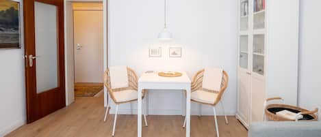 A dining area with a white table, two wicker chairs, a hanging light fixture, and a bookshelf with glass doors.