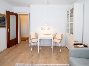 Et spiseområde med et hvidt bord, to fletstole, en hængende lampe og en bogreol med glaslåger.