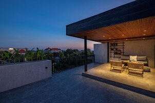 Un espace extérieur moderne, aménagé pour se détendre, avec un plafond en bois et une vue sur le paysage urbain au crépuscule.