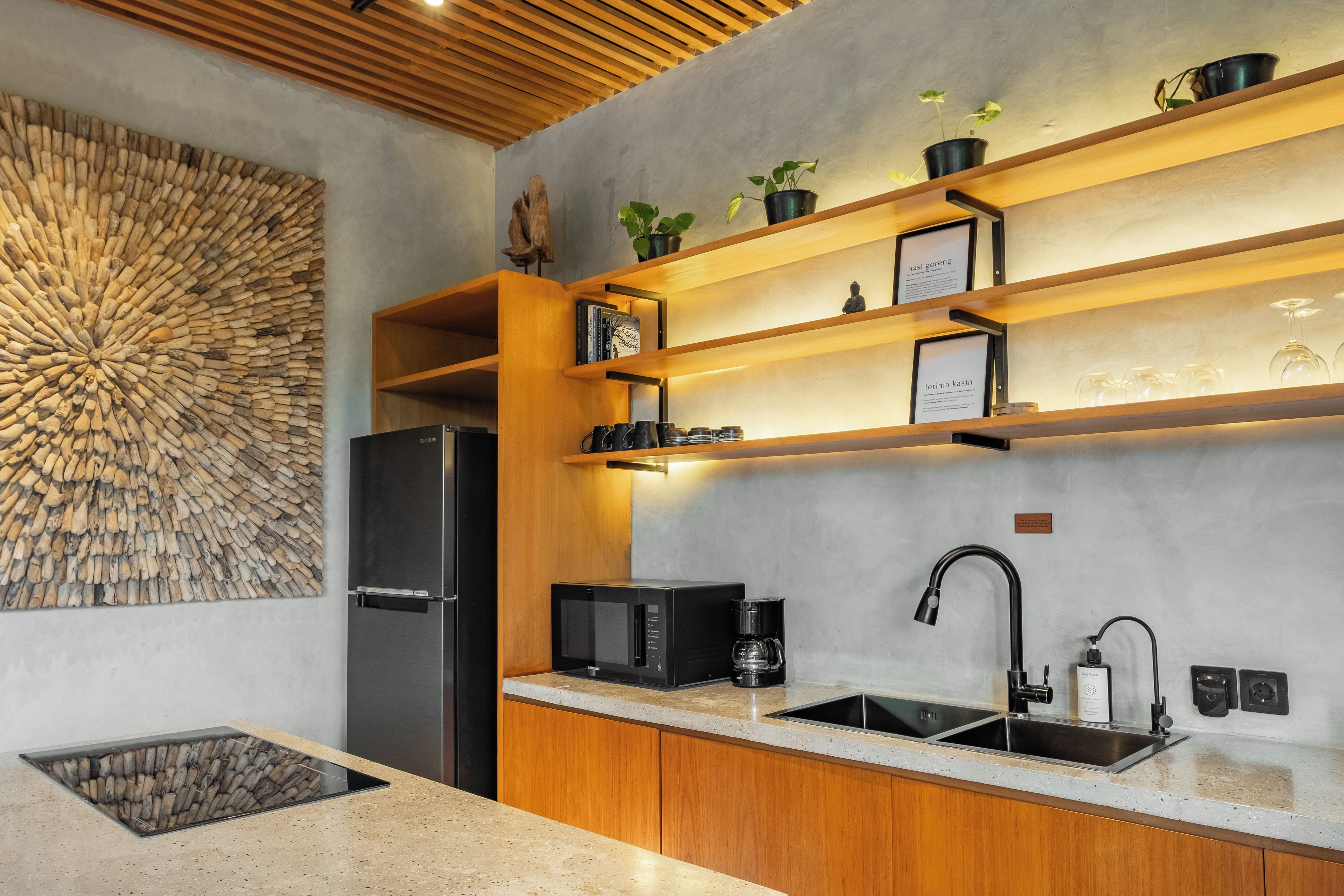 A modern kitchen with a built-in refrigerator, a microwave, and a coffee maker. There are wooden shelves with potted plants and a decorative wall piece.