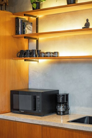 Una cocina con microondas integrado, cafetera y estantes con libros y tazas.