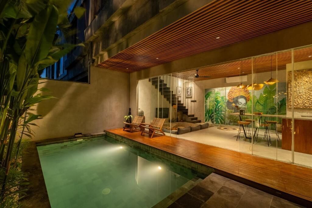 Un área de piscina interior moderna con terraza de madera, sillones de descanso y una escalera que lleva a una sala de estar con un mural.