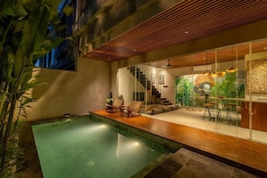 Ein moderner Poolbereich im Innenbereich mit Holzterrasse, Liegestühlen und einer Treppe zu einem Wohnbereich mit Wandgemälde.
