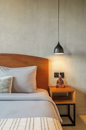 A bedroom with a bed, pillows, a bedside table with a Buddha statue, and a pendant light. - Villa Cek Ombak 2 (Badung)