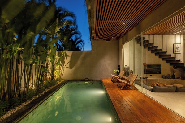 A modern outdoor pool area with a wooden deck, lounge chairs, and a staircase leading to an upper level. - Villa Cek Ombak 2 (Badung)