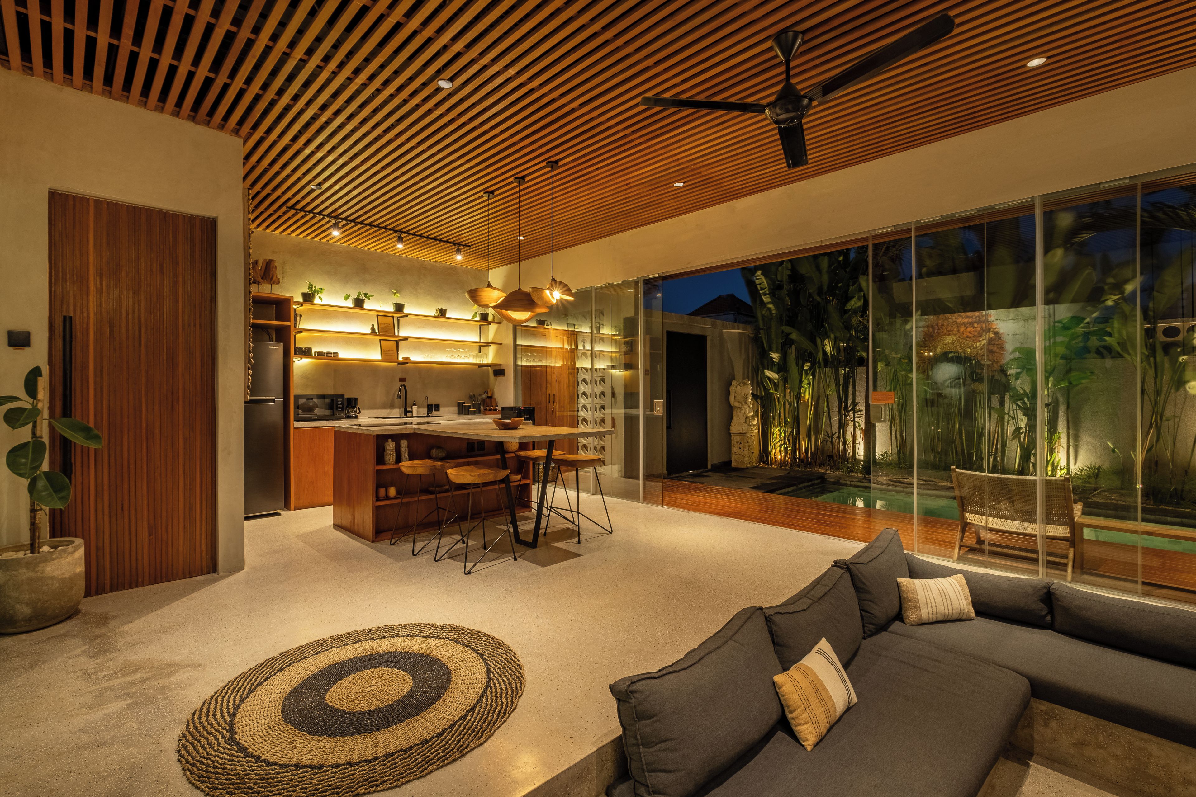 Un interior moderno con cocina, comedor y un amplio muro de cristal con vistas a un jardín.