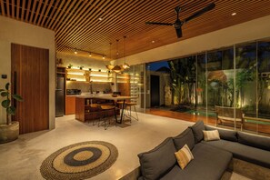 Un interior moderno con cocina, comedor y un amplio muro de cristal con vistas a un jardín.