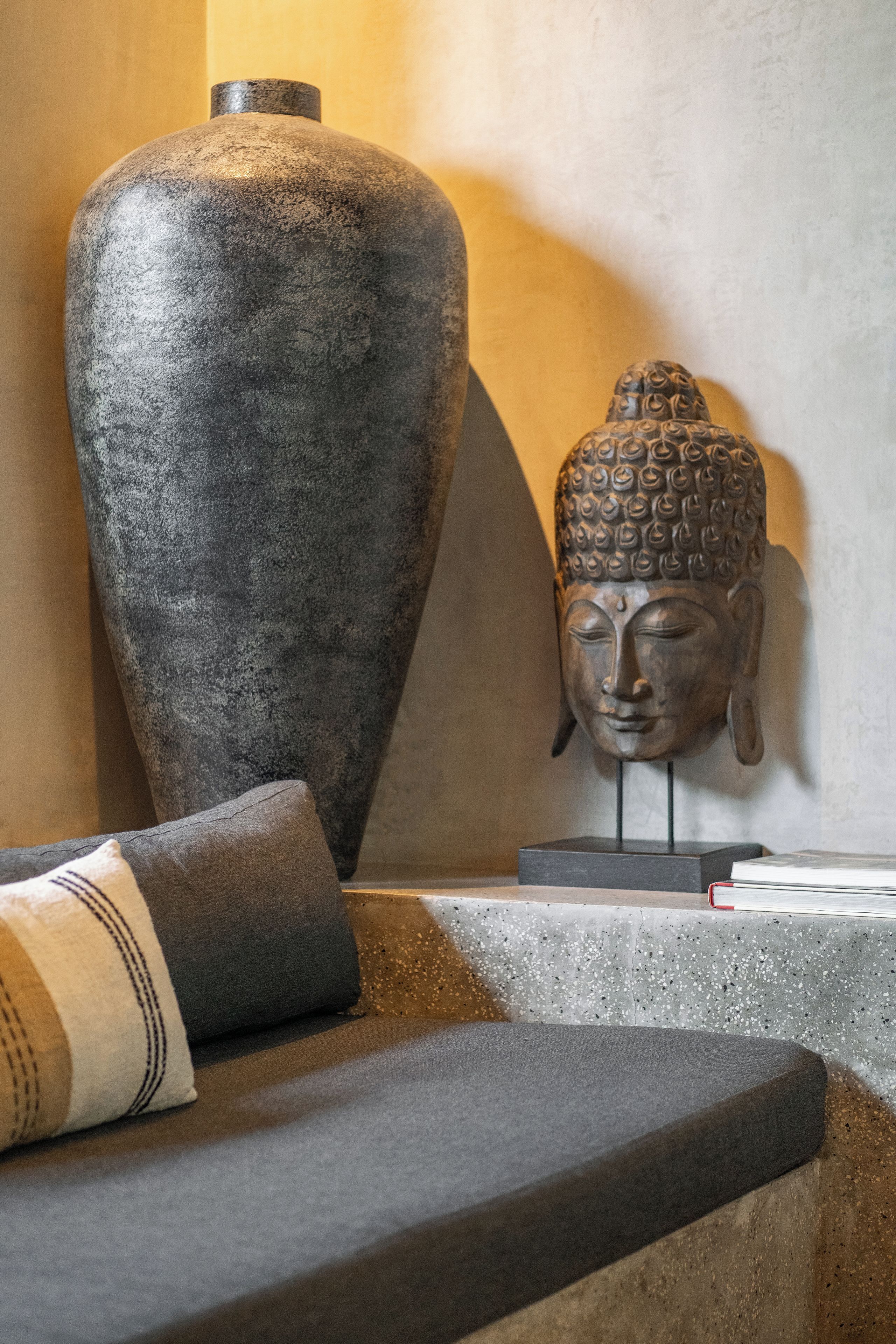 A stone sculpture of a Buddha head on a pedestal, a large stone vase, and a cushion on a ledge.