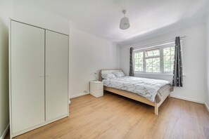 Ein Schlafzimmer mit einem Einzelbett, einem Kleiderschrank, einem Nachttisch und einem Fenster mit Vorhängen.