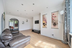 A spacious living room with a leather sofa, a flat-screen TV mounted on the wall, and two large wall-mounted paintings. - 2-br, Sleeps 4 With Garden Near Uni & Q E Hospital (Birmingham)