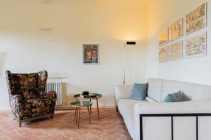 Ein Wohnzimmer mit einem floralen Sessel, einem weißen Sofa, einem kleinen runden Tisch mit einem Buch und einer Stehlampe.
