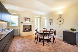 A modern kitchen with a dining area, featuring a fireplace, a clock, and a view of the outdoors. - Cozy Court | Relaxation and a Jacuzzi in the Monferrato Hills (Grazzano Badoglio)