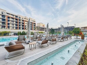 Ein Poolbereich auf dem Dach mit Liegestühlen und Sonnenschirmen, umgeben von modernen Gebäuden.
