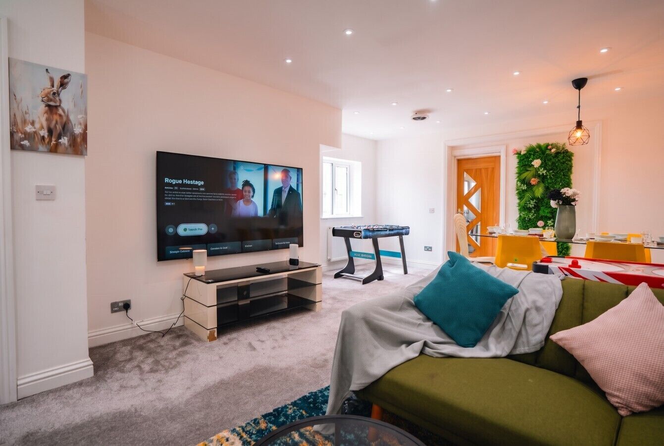 Een woonkamer met een flatscreen televisie, een groene bank, een bijzettafeltje en een decoratieve plant.
