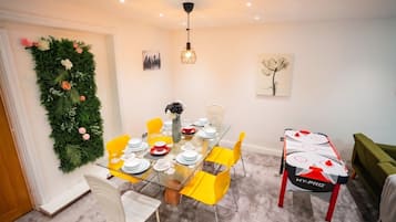 A dining area with a glass table, yellow chairs, and a green wall decoration.