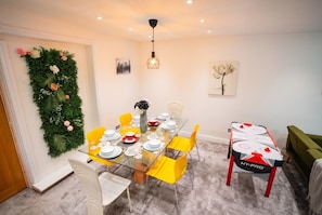 A dining area with a glass table, yellow chairs, and a green wall decoration.