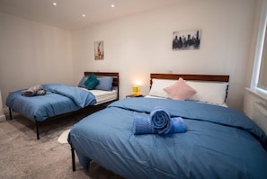 A hotel room with two beds, each with blue bedding and pillows, a nightstand with a lamp, and artwork on the walls.