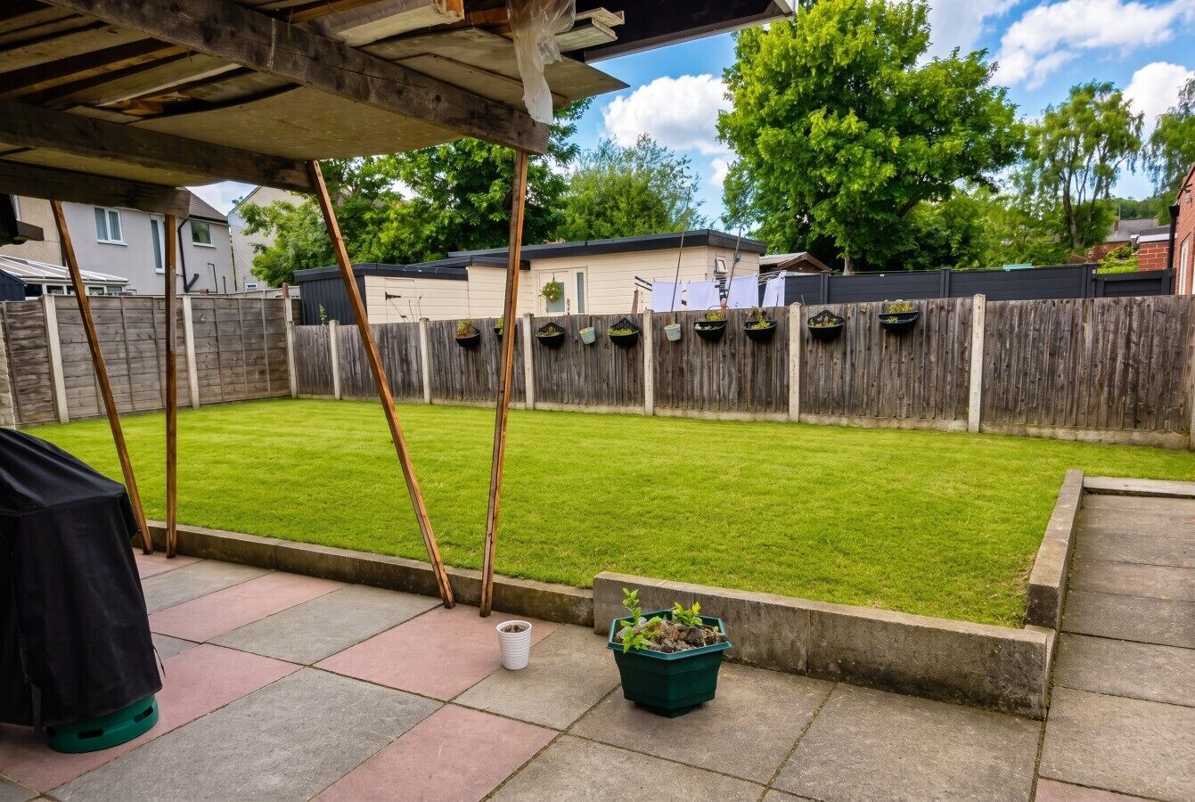 A backyard with a wooden fence, a grassy lawn, and a potted plant.