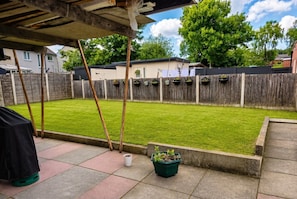 A backyard with a wooden fence, a grassy lawn, and a potted plant.