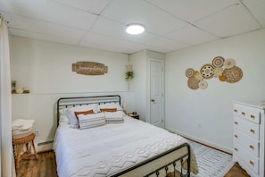 A bedroom with a bed, a dresser, a wall decoration, and a ceiling light.