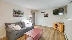 Ein Wohnzimmer mit grauem Sofa, einem roten Couchtisch, einem Fernseher und einer kleinen Holzeinrichtung mit Büchern.