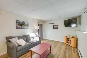 A living room with a grey sofa, a red coffee table, a television, and a small wooden cabinet with books. - Tranquil Woodland Retreat (Glenburn)