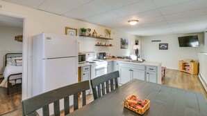 Eine kleine Küche mit Kühlschrank, Mikrowelle, Herd und Spüle. Ein Esstisch mit Stühlen und einer Bank lädt zum Verweilen ein. Die Wände sind weiß und die Decke ist mit Fliesen versehen.