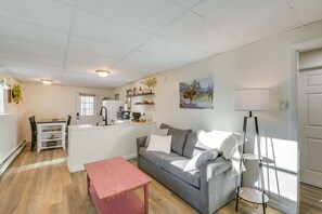 A modern living room with a grey sofa, a red coffee table, and a kitchen area with a white countertop and appliances. - Tranquil Woodland Retreat (Glenburn)