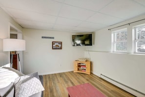 A room with a television mounted on the wall, a wooden cabinet, a sign reading 'MAINE,' and a window with a view of trees.