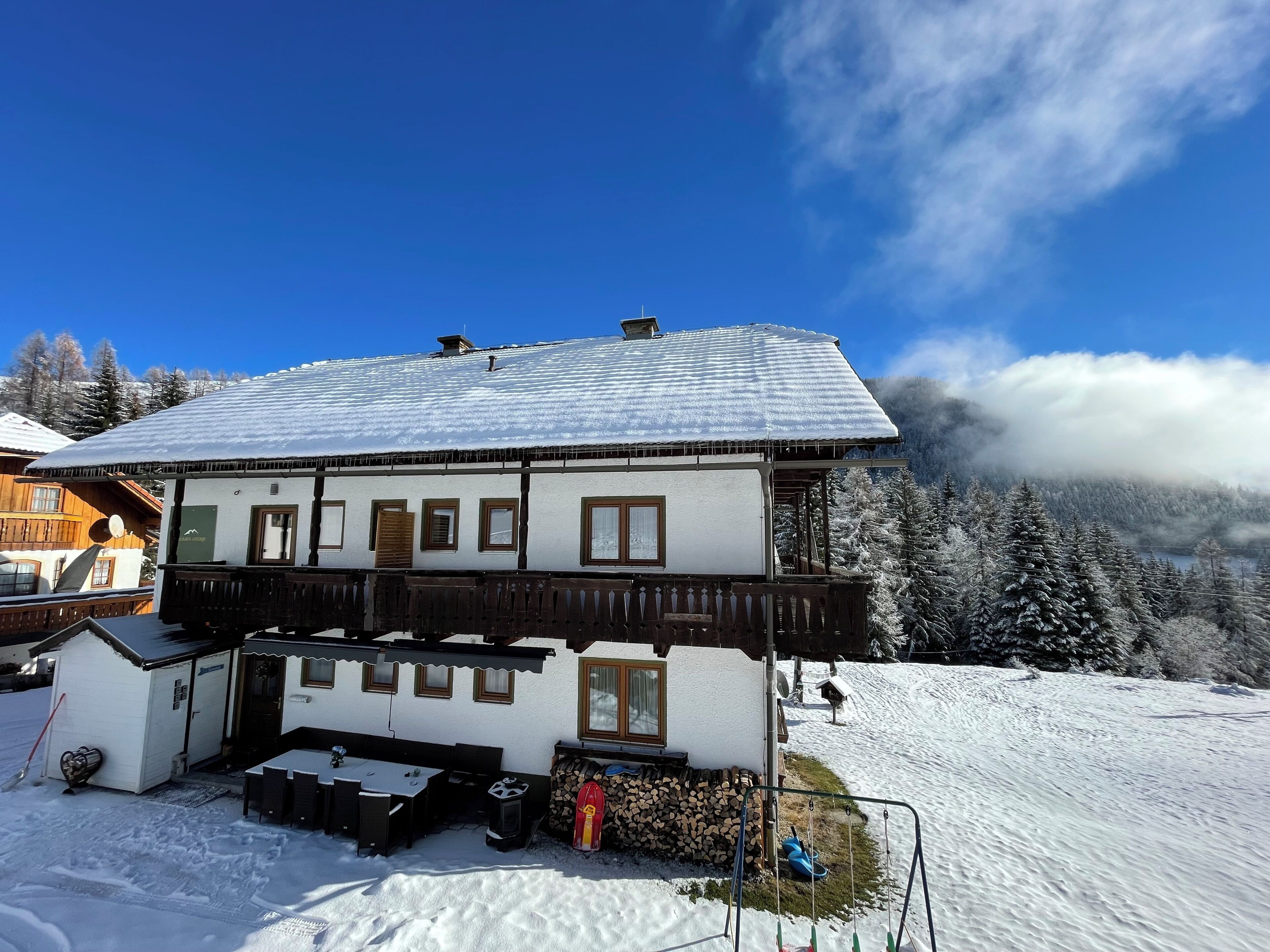 Uma cabana com varanda, deck de madeira e vista para árvores cobertas de neve.