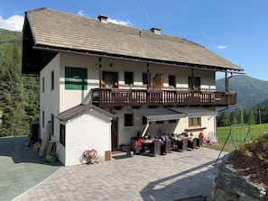 Ein zweistöckiges Gebäude mit einem Balkon, einem Schild mit der Aufschrift 'rockalm cottage' und einem gepflasterten Außenbereich mit Tischen und Stühlen.