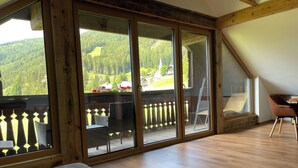 A room with a large sliding glass door leading to an outdoor balcony with a wooden railing and a view of a green landscape. - Nockalm Cottage Apartment 5 Kaiserburg Superior (Sankt Oswald)