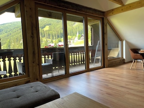 Ein Zimmer mit einer großen Schiebetür, die auf einen Balkon mit Holzgeländer und Blick ins Grüne führt.
