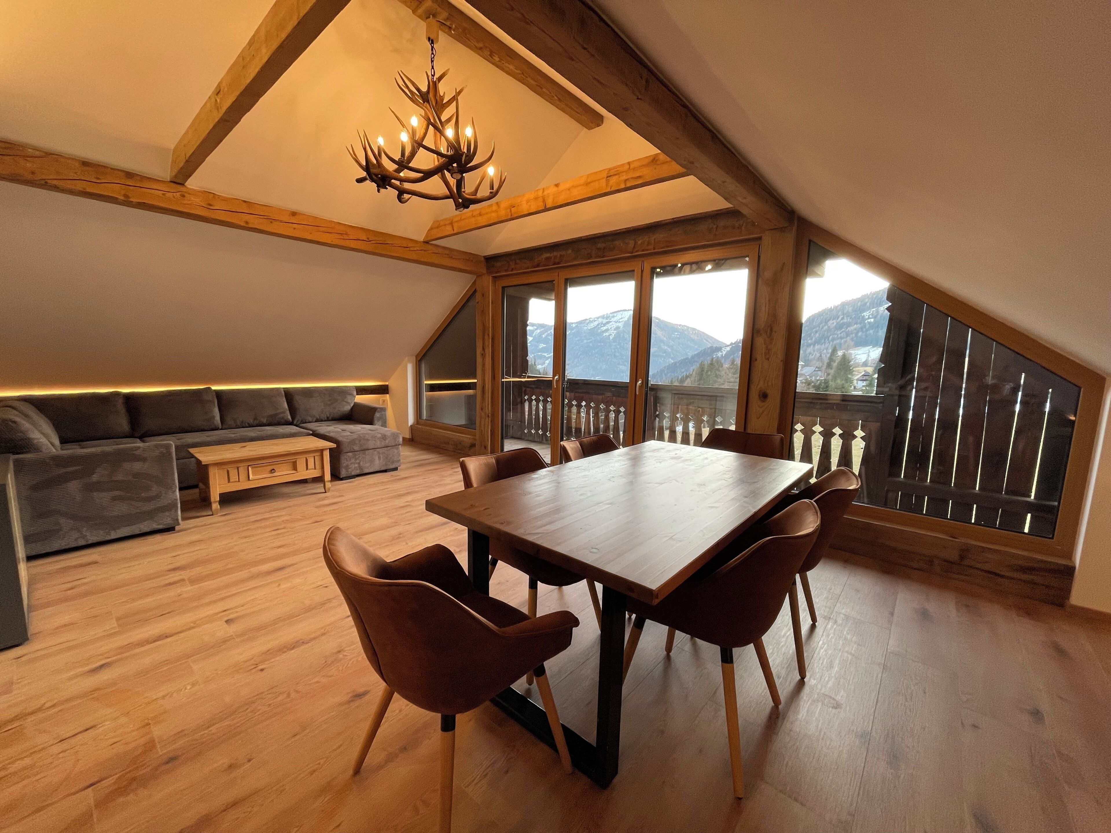 Ein Essbereich mit Holztisch und Stühlen, einer Couch und Blick auf Berge durch große Fenster.