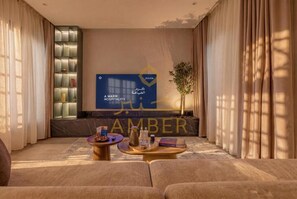 A hotel lobby with a large screen displaying the hotel's name, a reception desk, a seating area with sofas and tables, and a plant. - Amber Hospitality - AlQuds (Al Quds/ Riyadh)